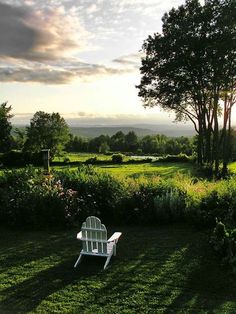 a white chair sitting in the middle of a lush green field under a cloudy sky