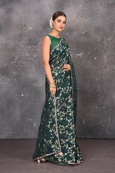 Indulge yourself with the elegance of Banaras with this dark green saree. The minute, metallic golden floral jaal design all over, gives the royal look to you & make you shine with richness and love at every occasion. Woven in fine silk with alluring designs and an urbane look. Perfect for weddings to cocktail evenings, this delightful piece is created in tones of tempting green. DISCLAIMER:- The shown stitched blouse on the model is for display purpose only. The saree comes with a matching blou Dark Green Saree, Saree With Border, Jaal Design, Kora Sarees, Royal Look, Fashion Journals, Green Saree, Traditional Fabric, Designer Saree