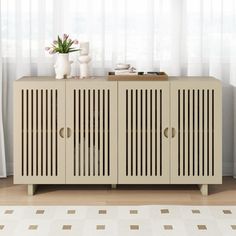 a sideboard in front of a window with white curtains and vases on top