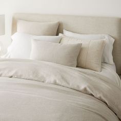 a bed with white linens and pillows in a neutral colored bedroom, along with a vase filled with flowers