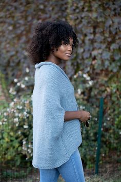 a woman walking down the street with her hand in her pocket, wearing jeans and a blue sweater