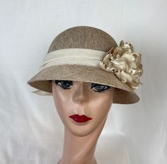 This vintage-inspired linen and cotton blend cloche hat which is trimmed with beige satin and tulle flowers, cream velvet leaves, and a 2 1/2 inch vintage linen and cotton blend ribbon. The inside band has a sizing cord and the hat will fit up to 22 5/8 inch head sizes. NOTE: Please check the head size before purchase, I am happy to answer any questions you may have. There will be a 20% restocking fee for all returned hats. Beige Cloche Hat For Wedding, Beige Cloche Hat For Church, Fitted Beige Cloche Hat For Church, Cream Cloche Hat With Short Brim For Church, Fitted Beige Cloche Hat, Beige Brimmed Cloche Hat For Church, Fitted Beige Cloche Mini Hat, Cream Gatsby Style Hat, Adjustable Cream Gatsby Hat