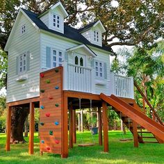 a tree house with a climbing wall and slide in the grass next to a playground