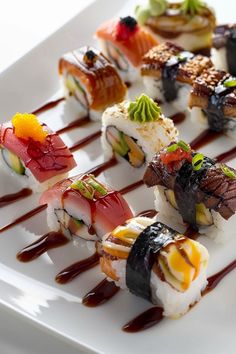 a white plate topped with different types of sushi on top of sauce covered chopsticks