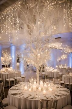 a white tree with candles in it is surrounded by round tables and chandeliers