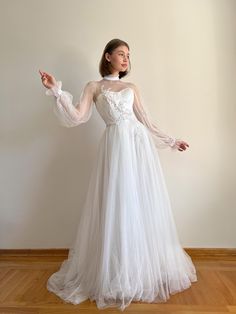 a woman in a long white dress standing on a wooden floor with her arms outstretched