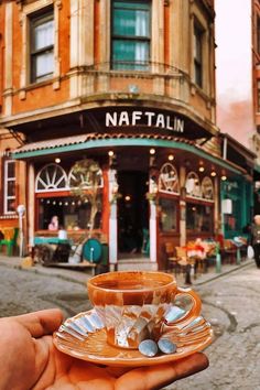 a person holding up a cup and saucer in front of a building