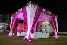 a decorated stage with pink drapes and white couches on the lawn at night