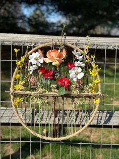 a basket with flowers in it sitting on a wooden bench next to a wire fence