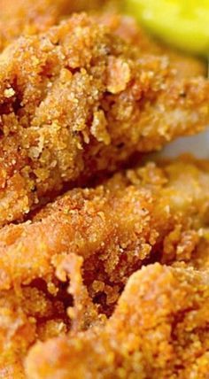 some fried food on a white plate with pickles and breadcrumbs in the background