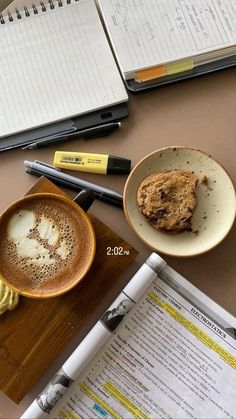 there is a cup of coffee and a cookie on the table next to a notebook