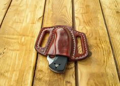 a brown leather case with a knife inside it on a wooden table next to a cell phone