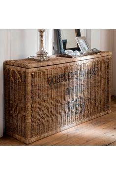 a wicker chest with writing on it in front of a mirror and wooden floor