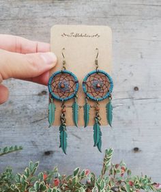 a pair of earrings with feathers hanging from it's earring hooks in front of a wooden background