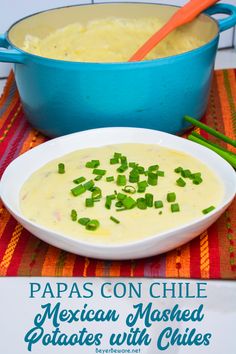 a bowl of mexican mashed potatoes with chives on the side next to a large blue casserole dish