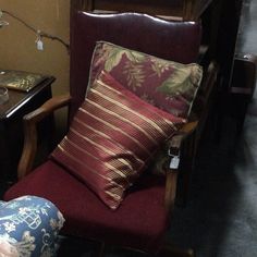 a red chair with two pillows on it next to a table and other furniture in a room