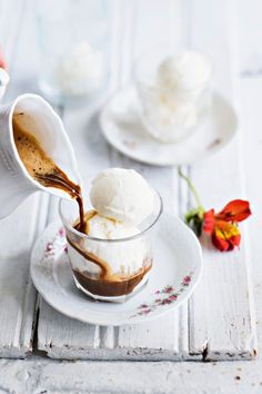 someone pouring ice cream into a small glass bowl on a white plate with flowers in the background