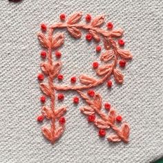 an embroidered letter with red beads and leaves