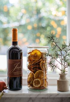 a bottle of wine sitting on top of a window sill next to a vase filled with orange slices