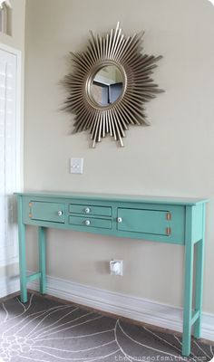 a blue console table in front of a wall with a sun mirror on it's face