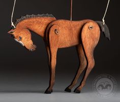 a wooden toy horse is hanging from a string on a black background with an inscription below it