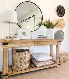 a wooden table topped with a mirror next to a lamp and wicker basket filled with pillows