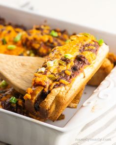 a casserole dish with meat, cheese and green onions in it next to a wooden spoon