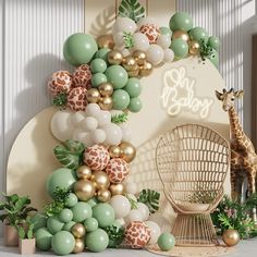 a giraffe standing next to a wall with balloons and greenery on it