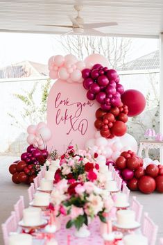 a table topped with lots of pink and red balloons next to a heart shaped sign