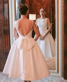 a woman standing in front of a mirror wearing a white dress