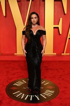 a woman in a black dress standing on a red carpet with her hands on her hips