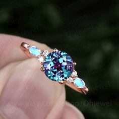 a person is holding an engagement ring with blue and pink stones