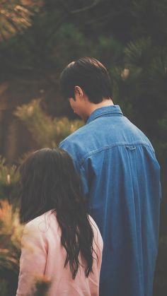 a man and woman standing next to each other in front of pine trees, looking at the sky