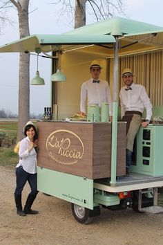 two men and a woman standing in the back of a food truck with an awning