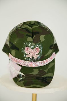 Make a fashion statement with this unique BEADED BOW CAMO TRUCKER HAT! Show off your style with the adjustable snapback and the camo pattern, pink beaded ribbon band, beaded bow patch, and a whole lotta' pink and white feathers with a hint of silver glitter. Get ready to turn heads! This is a made-to-order item. All customized orders are currently shipping within 14 business days. To receive item quicker, expedited shipping is available at checkout. Adjustable Camouflage Hat For Spring, Pink Adjustable Hat With Ribbon, Adjustable Pink Hat With Ribbon, Pink Adjustable Ribbon Hat, Adjustable Camouflage Snapback Hat With Visor, Camouflage Adjustable Visor Snapback Hat, Custom Baseball Hats, Beaded Ribbon, Camo Trucker Hat