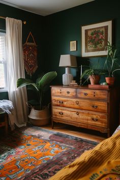 Cozy sage green bedroom decor with vintage wooden dresser, lush plants, and vibrant area rug for a touch of inspiration. Forest Green Bedroom Decor Ideas, Dark Green Brown Bedroom, Green And Rust Bedroom Ideas, Dark Green Walls Bedroom Aesthetic, Dark Green Mid Century Bedroom, Bedroom Dark Wood Floor, Dark Sage Green Bedroom, Sage Green Bedrooms, Green Bedroom Inspirations