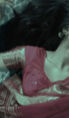 a woman laying down with her hair blowing in the wind, wearing a pink sari