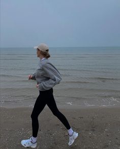 a woman running on the beach in front of the ocean with her head turned to the side