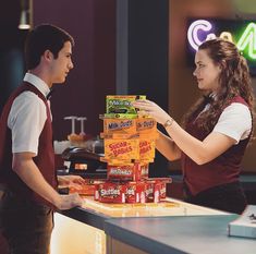 a man and woman standing in front of a counter with boxes on top of it