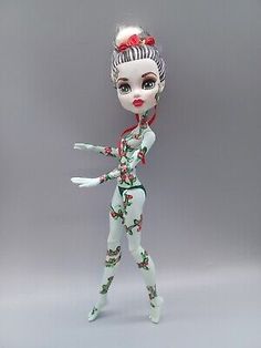 a white doll with red flowers on her head and arms, wearing a green body suit