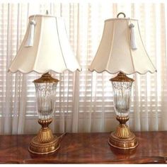 two glass lamps sitting on top of a wooden table next to a white lamp shade