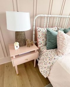 a bed with pink and green pillows on it next to a night stand that has a white lamp