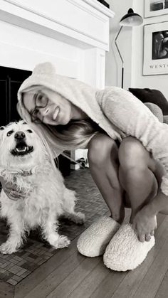 a woman kneeling down next to a white dog on top of a hard wood floor