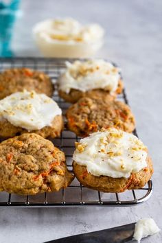 carrot muffins with cream cheese frosting on a cooling rack next to a knife