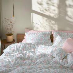 an unmade bed with pink and blue comforters in a white room next to a window