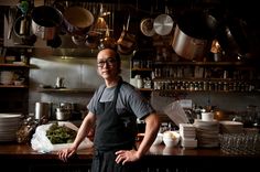 a man standing in front of a counter with lots of pots and pans hanging from the ceiling