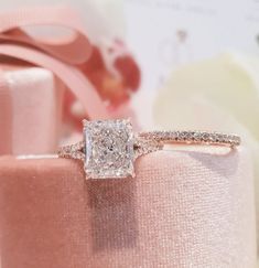 a diamond ring sitting on top of a pink velvet box with a ribbon around it