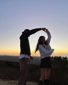 two people standing on top of a hill at sunset