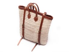 a straw bag with leather handles and straps on the bottom, sitting against a white background