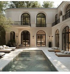 an outdoor swimming pool in front of a large white house with lots of windows and doors